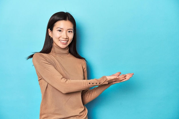 Young Asian woman in brown turtleneck holding a copy space on a palm