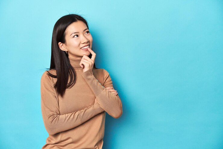 Photo 茶色のタートルネックを着た若いアジア人女性が、コピースペースを見て何かについて考えながらリラックスした