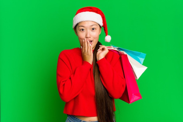 Молодая азиатка покупает подарки на рождество на зеленом цветном фоне