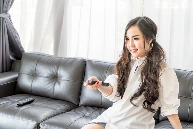 若いアジアの女性、テレビのチャンネルを変更する