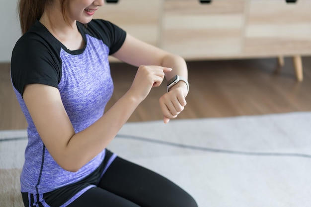 젊은 아시아 여성이 집에서 운동을 한 후 손목 시계에서 운동 시간과 심박수를 확인하고 있습니다.