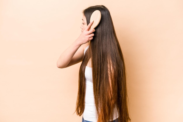 Young asian woman combing her hair isolated on beige background