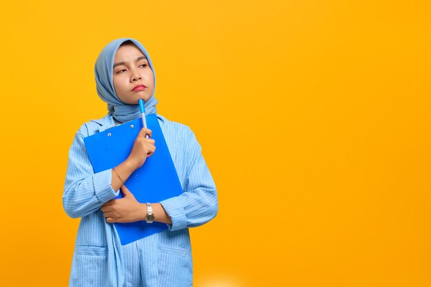 Young Asian woman concentrated writing notes planning creating strategy over yellow background