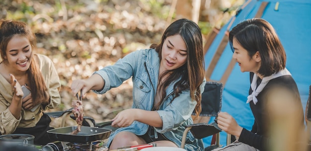 La giovane donna asiatica che cucina e la sua amica si divertono a preparare il pasto in padella. parlano e ridono insieme divertendosi mentre si accampano nel parco naturale