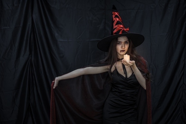 Young asian woman in costume witch and hold candle on black\
cloth background of halloween concept. portrait of teen woman\
dressed up as witch for celebrate halloween festival.