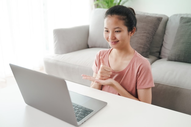 Young Asian woman deaf disabled using laptop computer for online video conference call learning and communicating in sign language.