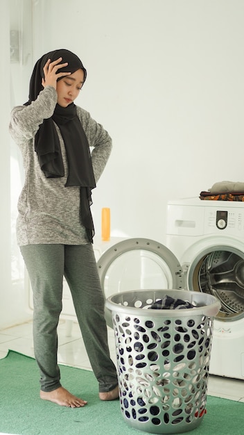 Young asian woman dizzy looking at dirty clothes basket at home