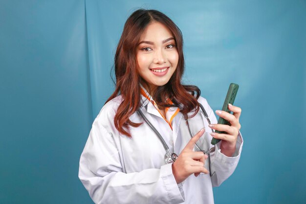 Young Asian woman doctor is pointing and showing green screen or copy space on her smartphone