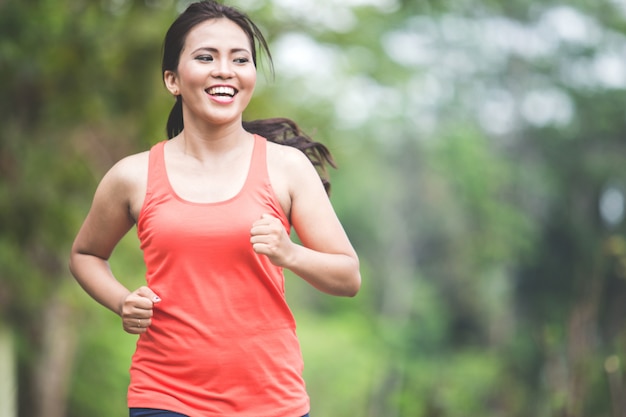 Молодая азиатская женщина делая тренировку напольную в парке, jogging