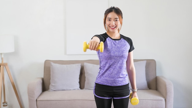 Молодая азиатская женщина делает упражнения и поднимает гантели, чтобы тренироваться, тренируя сильные руки дома