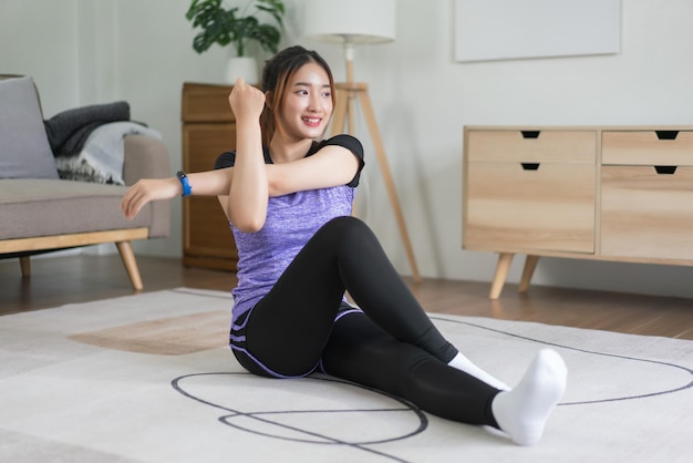 Молодая азиатка занимается физическими упражнениями, растягивает руки на полу для тренировок, здоровый образ жизни дома.