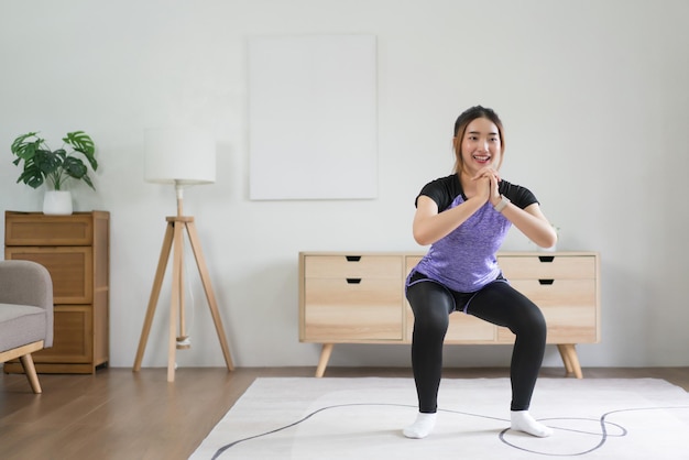 젊은 아시아 여성이 집에서 건강한 생활 방식을 위해 바닥에 앉아 운동을 하고 있습니다.