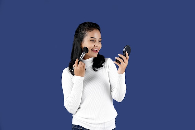 Young Asian woman doing makeup and holding a mirror