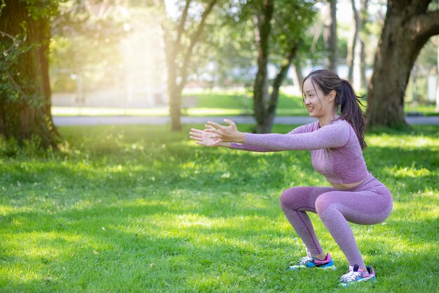 自然公園でヨガフィットネスエクササイズをしている若いアジア人女性、健康またはウォーミングアップのためのエクササイズ、新鮮な空気、または日光の下で公園の緑の木で酸素。