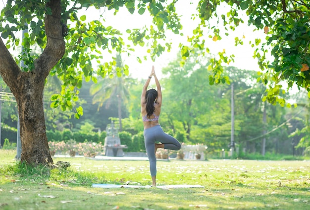 写真 公園の木の下でヨガをやっている若いアジア女性