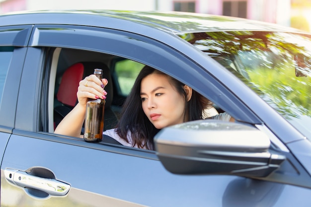 Young asian woman drinking beer while driving a car