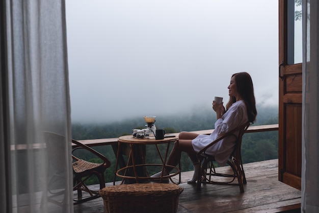 Una giovane donna asiatica che beve caffè a goccia e guarda una bellissima vista della natura in una giornata nebbiosa