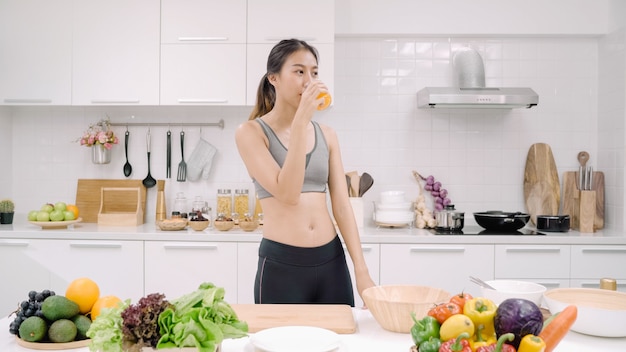 young asian woman drinking orange juice in the kitchen