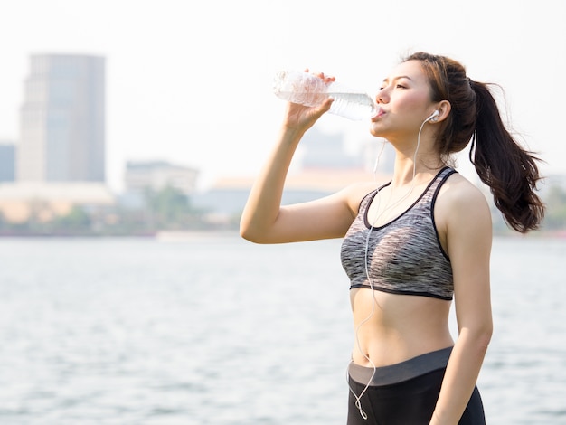 Young asian woman drinking water during workout, running, jogging