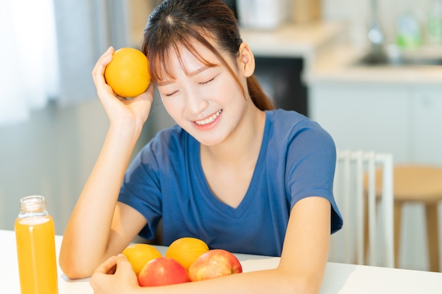 그녀의 부엌에서 과일과 함께 아침을 먹는 젊은 아시아 여자
