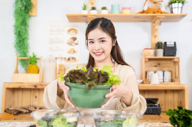 샐러드 야채와 함께 건강에 좋은 음식을 먹는 젊은 아시아 여성 아름다운 실내 주방의 식료품 저장실에 앉아 있는 여성