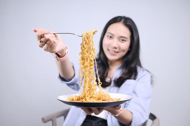 Foto giovane donna asiatica che mangia noodle con la forchetta e la mostra alla telecamera focalizzazione selettiva focalizzazione sui noodle