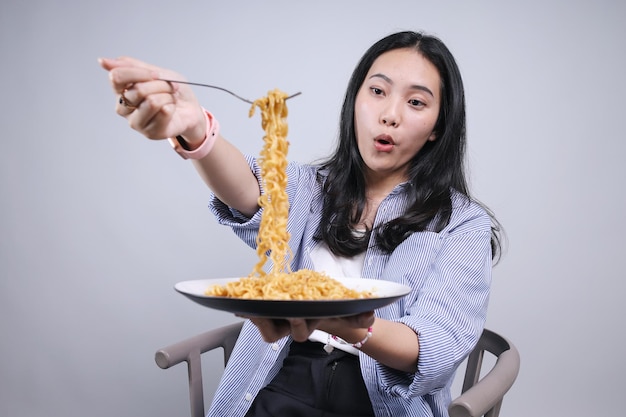 Foto giovane donna asiatica che mangia noodles e lo mostra alla telecamera con un'espressione di sorpresa