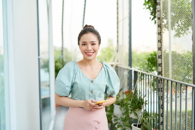 자연을 즐기고 발코니에서 전화를 사용하는 젊은 아시아 여성