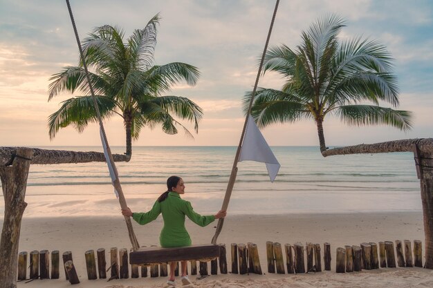 Молодая азиатская женщина наслаждается деревянными качелями на пляже на закате