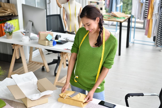 Young Asian woman entrepreneur / fashion designer working in studio and packing and sending product