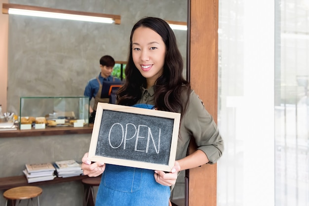 Молодой предприниматель азиатских женщин, показывая открытый знак в передней двери кафе