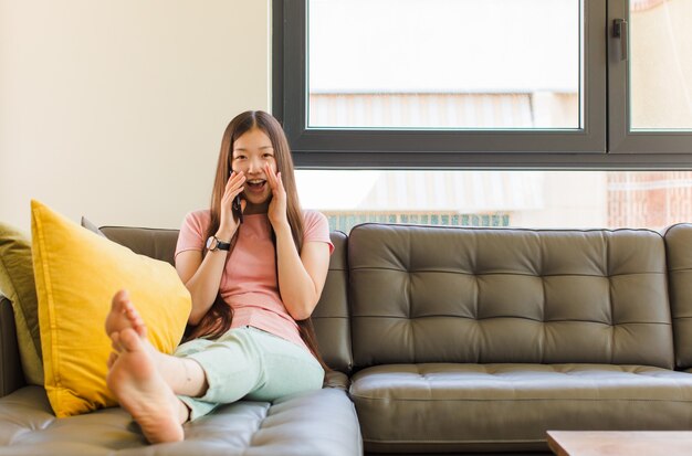 Young asian woman feeling happy, excited and positive, giving a big shout out with hands next to mouth, calling out