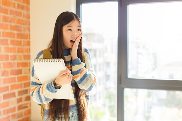 Young asian woman feeling happy, excited and surprised, looking to the side with both hands on face