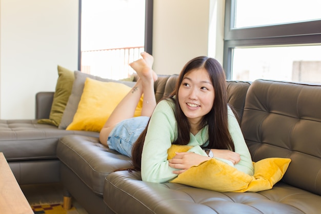 Young asian woman feeling happy, proud and hopeful, wondering or thinking, looking up to copy space with crossed arms