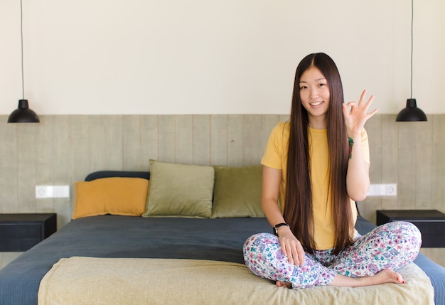 Young asian woman feeling happy, relaxed and satisfied, showing approval with okay gesture, smiling