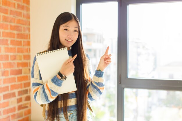 Young asian woman feeling joyful and surprised, smiling with a shocked expression and pointing to the side