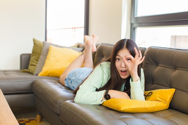 Young asian woman feeling shocked, amazed and surprised, holding glasses with astonished, disbelieving look