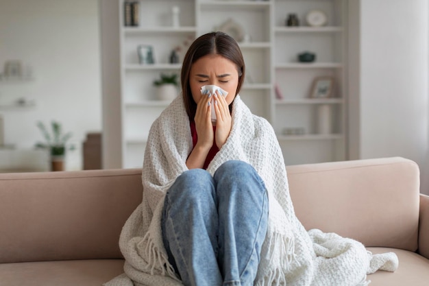 Young asian woman feeling unwell at home sneezing into tissue