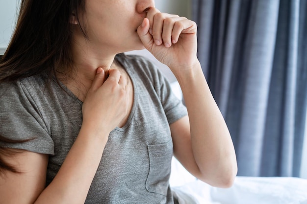 若いアジアの女性は寝室で気分が悪く咳をしている