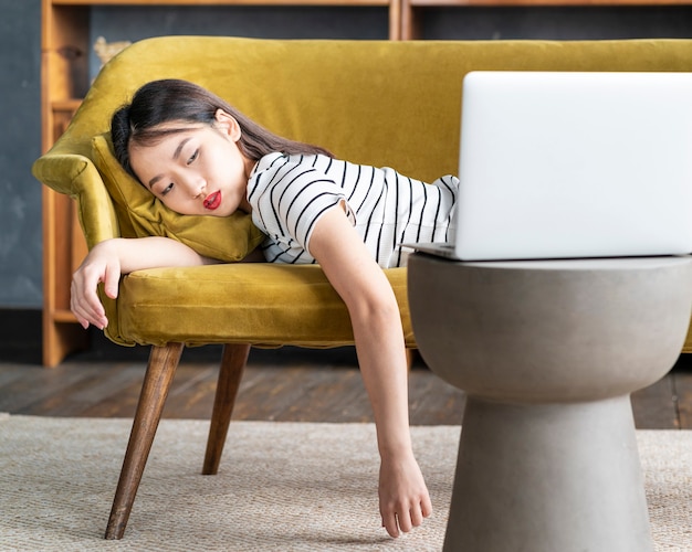 Молодая азиатская женщина заснула на диване перед ноутбуком