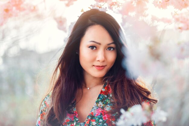 春に開花する桜の木の前で花のパターンのドレスを着た若いアジア人女性