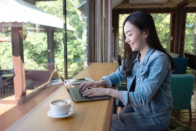 젊은 아시아 여성 프리랜서가 커피숍에서 노트북으로 작업하고 있습니다.