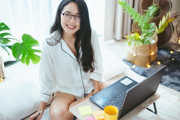 若いアジアの女性のフリーランスの仕事のビジネスは、自宅でラップトップに取り組んでいます。