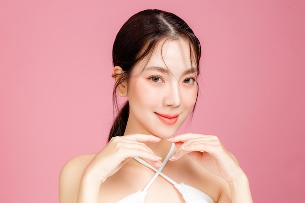 Young Asian woman gathered in ponytail with natural makeup on face have plump lips and clean fresh skin wearing white camisole on isolated pink background Portrait of cute female model in studio