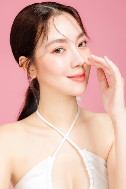 얼굴에 자연스러운 화장을 한 포니테일로 모인 젊은 아시아 여성은 통통한 입술과 격리된 분홍색 배경에 흰색 캐미솔을 입은 깨끗하고 신선한 피부를 가지고 있습니다 스튜디오에 있는 귀여운 여성 모델의 초상화