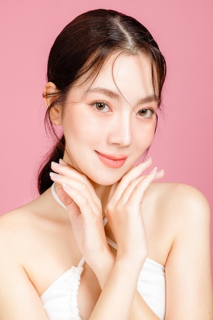 Young Asian woman gathered in ponytail with natural makeup on face have plump lips and clean fresh skin wearing white camisole on isolated pink background Portrait of cute female model in studio