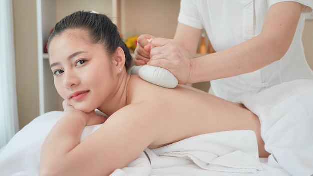 Photo young asian woman getting spa massage with thai herbal ball hot compress massage at beauty spa salon. relaxing massage for health