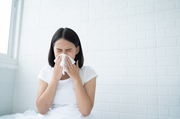 Photo young asian woman got nose allergy, flu sneezing nose sitting at bed in bedroom