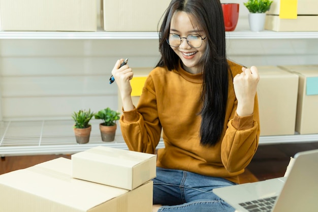 Photo young asian woman happy with sales surpassing target and raising her arms shopping online concept