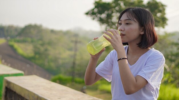 若いアジアの女性は、朝ジョギングした後、飲酒と休憩を持っています